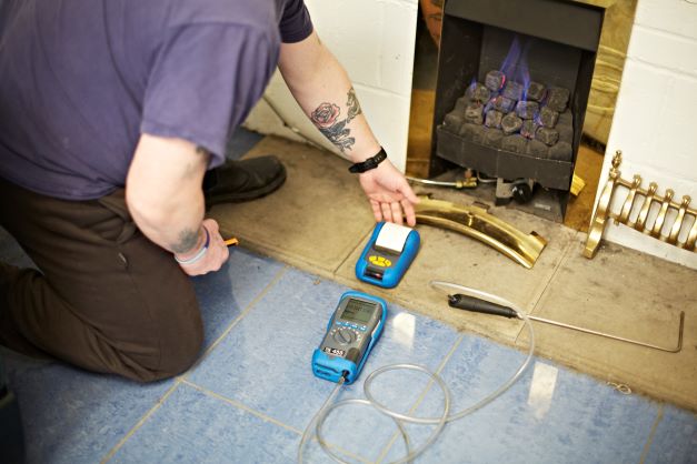 Featured image for article "What does the future hold for gas engineers?' shows gas engineer kneeling in front of a gas fire carrying out maintenance