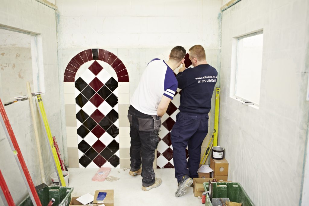 Tiling work bay at Able Skills where an instructor is showing a student how to hang wall tiles into a decorative arch design