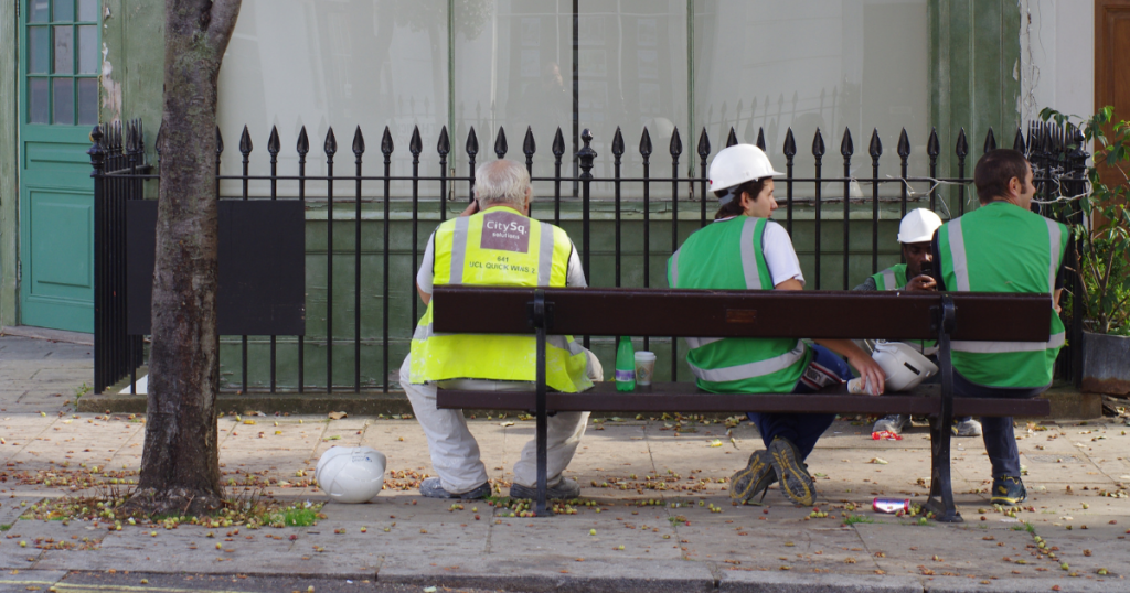 Featured image for article about mental health in the construction the industry shows group of four construction workers sitting on a bench, wearing hi-viz jackets and hard hards