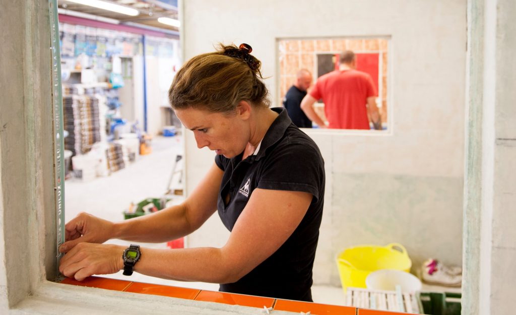 Featured image for article about diversity in construction and why we need more women in the trades. Image shows female tiler preparing a window surround for tiling.