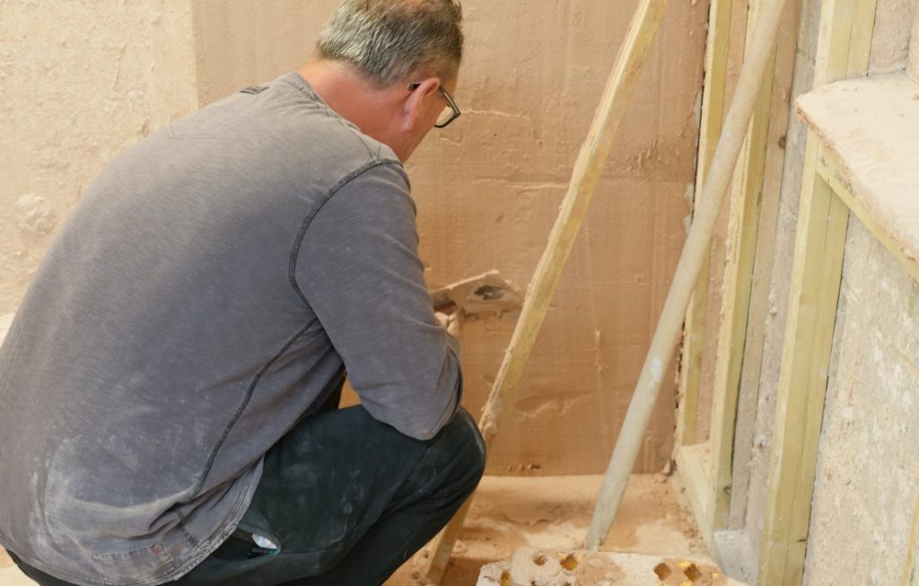 A plastering student at Able Skills is crouched down applying fresh plaster to a wall