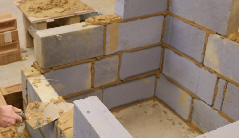 Block wall in construction, a hand holding a trowel laying on wet mortar is in the bottom left