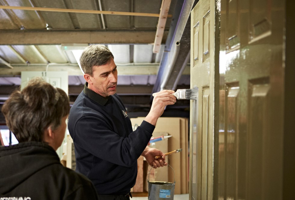 Able Skills instructor demonstrating painting a wooden door in the Able Skills construction training centre