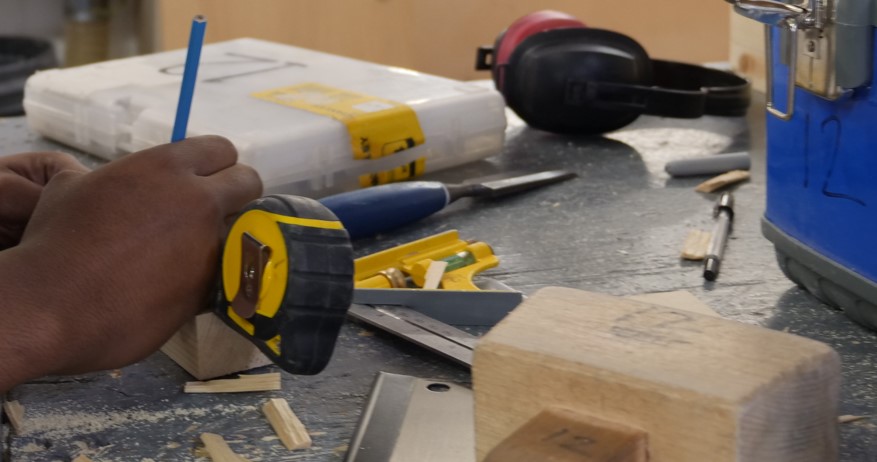 Tape measure, ear defenders and carious tools and wood on a workbench at Able Skills