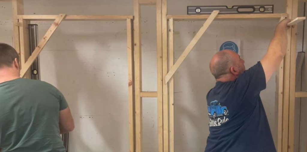 Two people building a wooden framework that could be for a partitioning or stud wall