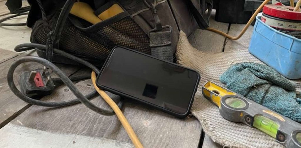 Smart phone placed on wooden floor boards, next to a spirit level, cables and a tool bag