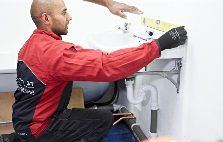 Trainee plumber installing a sink using a spirit level 