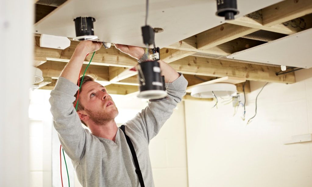 Person running electric wiring for lighting in a ceiling
