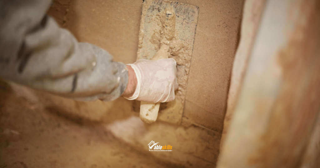 A hand applying wet plaster to the wall using a tool