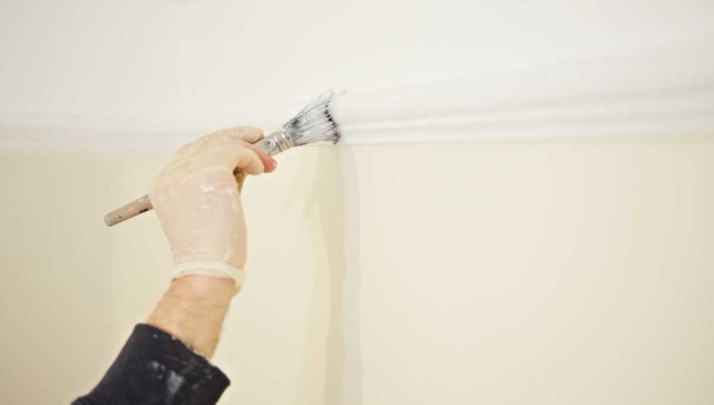 A hand holding a paint brush painting architrave white