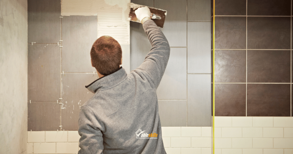 Person applying tile adhesive to a wall and hanging grey and brown tiles.