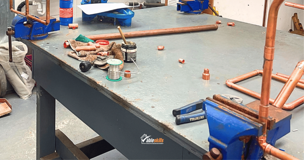 A workbench with copper pipes, vice, flux and solder