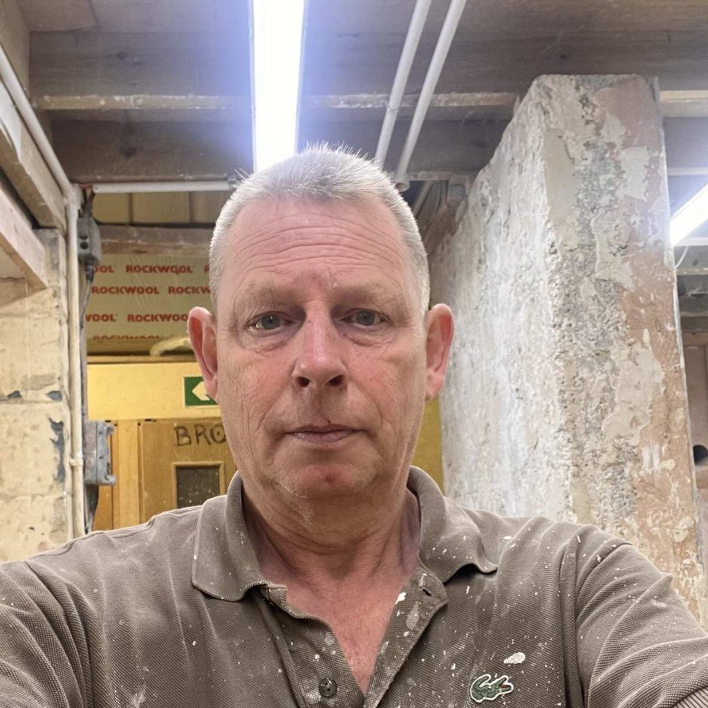 Stephen is facing the camera, behind him are the walls of the plastering and rendering workshops at Able Skills