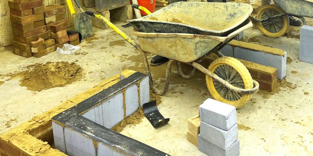 A wheelbarrow next to bricks and breezeblocks being built into a corner wall