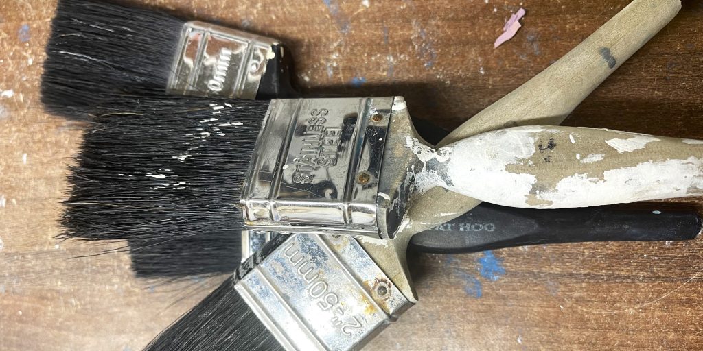 Three paintbrushes on a wooden worktop surface