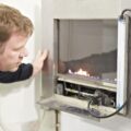 A gas engineer is looking at a gas fire. The controls of the fire are open and there are flames behind the glass