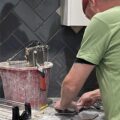 Two people are cutting tiles to install a kitchen splashback