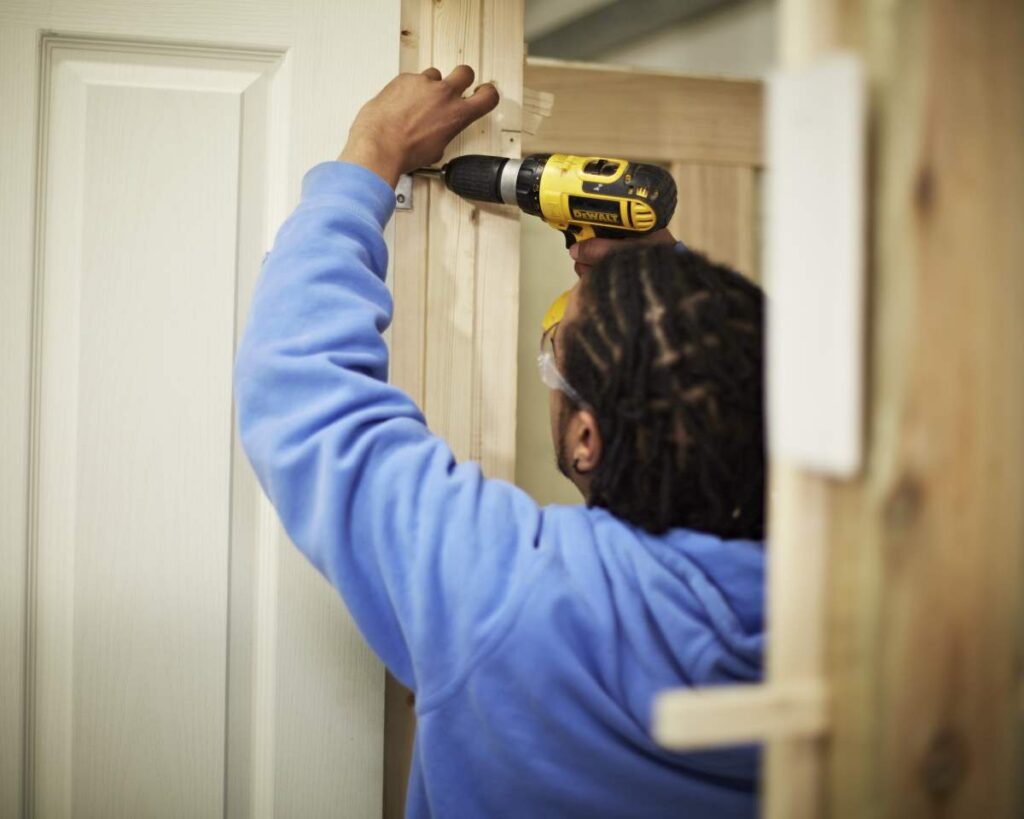 Person using a driver to fix a hinge onto a door frame.