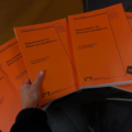 Orange 18th edition books on a desk. A hand is holding one copy