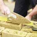 An unknown person applying mortar to bricks using a trowel while holding a level. They are building a wall,