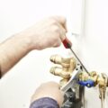 Person using an adjustable wrench and screwdriver to adjust plumbing valves