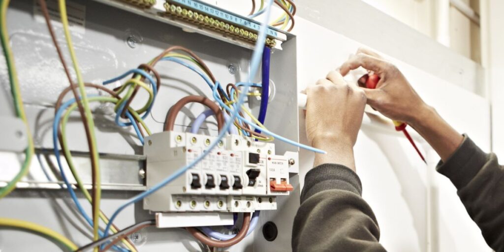 A pair of hands are working on wiring in a fusebox