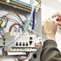 A pair of hands are working on wiring in a fusebox