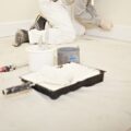A decorator is kneeling down prepping skirting board for painting. A paint tray and roll are on the floor.