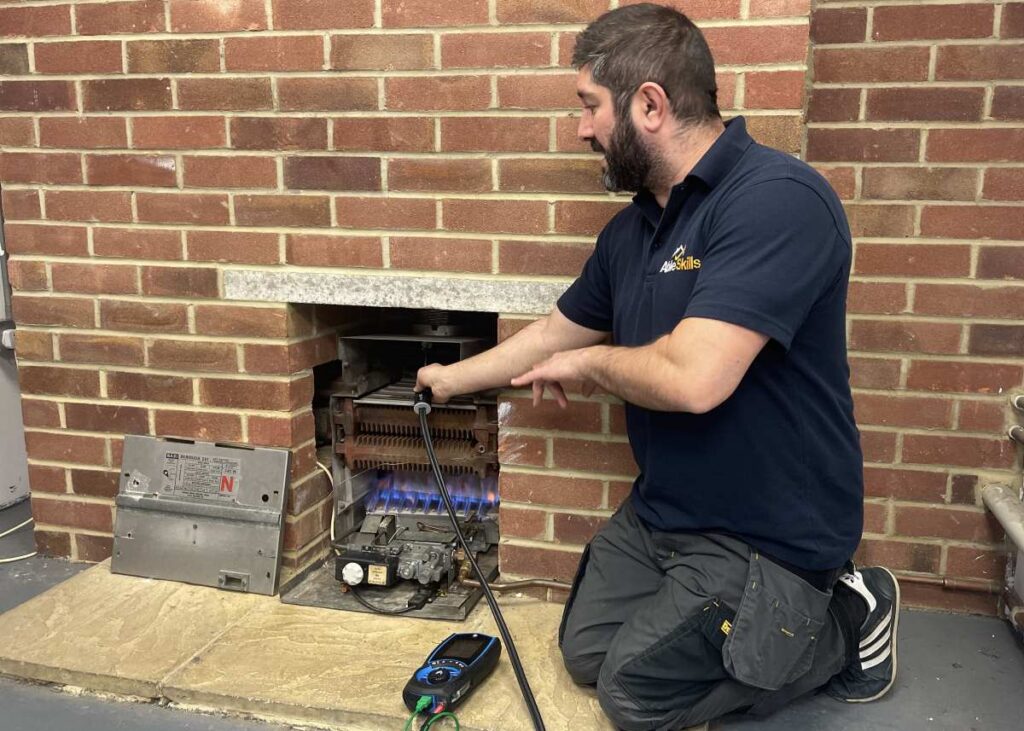 An Able Skills gas instructor is kneeling in front of a gas fireplace using a gas analyser