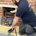 An Able Skills gas instructor is kneeling down in front of a gas fireplace using a gas analyser instrument