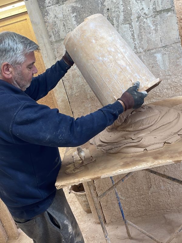 An Able Skills plastering instructor prepares wet plaster by tipping it from a bucket onto a table before.